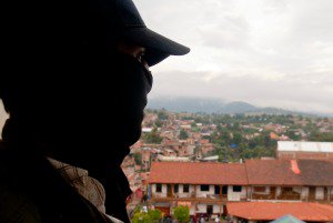 A masked man, member of the community police of Cherán, looks out from a church tower over the main square.
