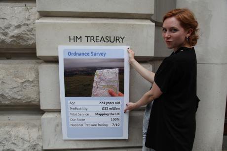 A woman holding a Top Trumps card showing the value of the Ordnance Survey.