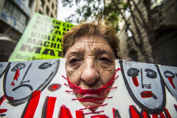 A woman with her head inside a protest banner at a demonstration in São Paulo against cuts to victims of violence against women