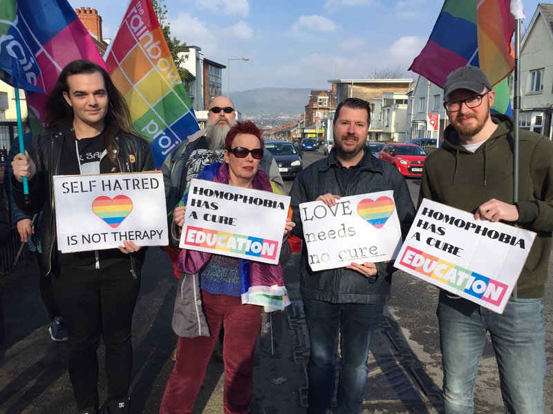 protestors against conversion therapy hold signs and pride flags