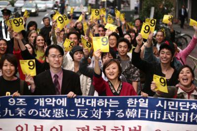 Crowd of young people behind a banner holding up yellow sheets with &#39;9&#39; written on them.