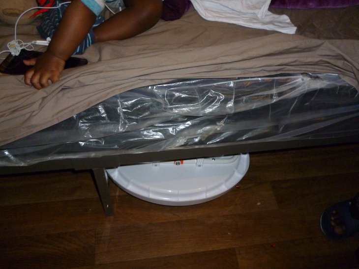 Mattress wrapped in plastic. Child lies on mattress playing with phone.
