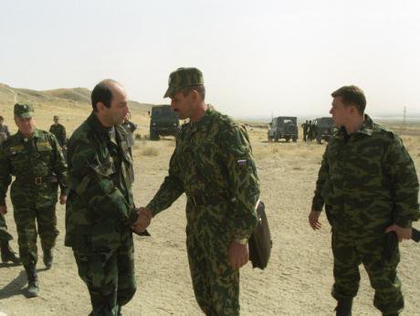 Two men in military uniform shake hands in a desert. 