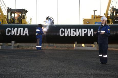 Russian workers stand in front of a piece of pipeline reading 'the power of Siberia.'