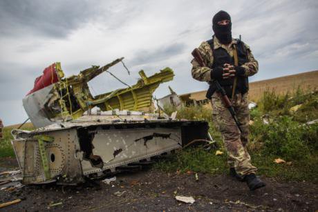 A rebel in a balaclava stands by a ruined piece of MH17.