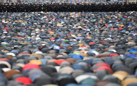 Мусульмане стоят на коленях во время молитвы перед полицейским кордоном.