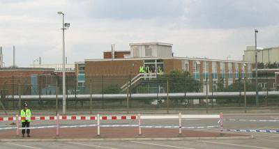 Industrial building with policeman standing outside. Workers standing on a balcony.