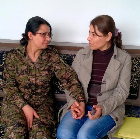 Two women sit holding hands, one of them in combat fatigues.