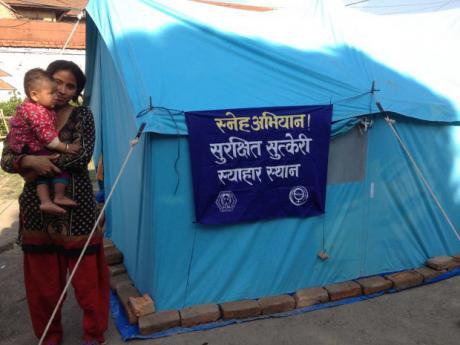 Woman holds child beside an aid tent