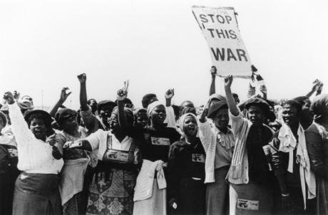 Women, arms raised, protesting. One with a sign &#39;Stop this war&#39;.