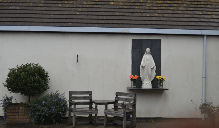 image of chairs and statue of the Virgin Mary outside white building