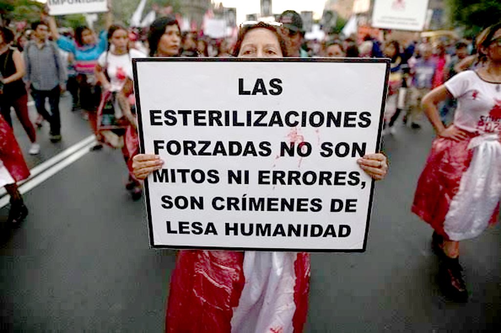 Mulher em protesto segurando um cartaz que lê: 'As esterilizações forçadas não são mitos ou erros, são crimes contra a humanidade'