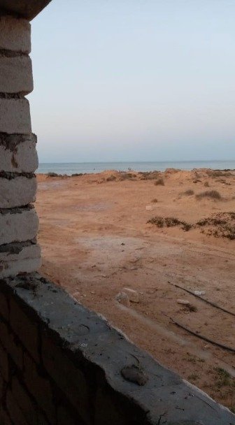 A cinderblock house in a desert landscape with the sea in the distance