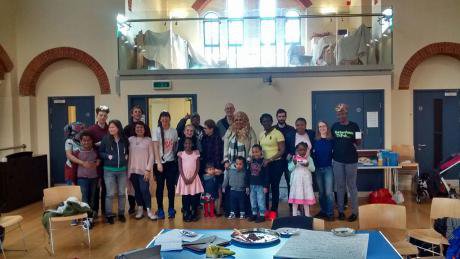 Smiling men, women and small children stand in centre of a church hall.