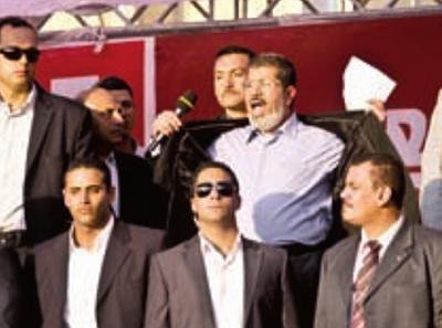 President Morsi surrounded by body guards, opening his jacket to show his shirt.
