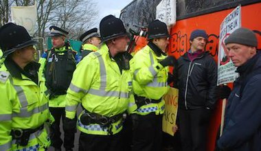 Police film and speak to a man with a placard stood against a big red bus