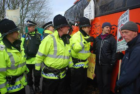 Police film and speak to a man with a placard stood against a big red bus