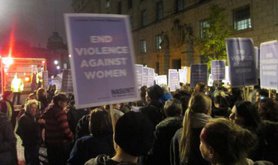 Women marching in the dark with an 'End Violence Against Women' placard visible