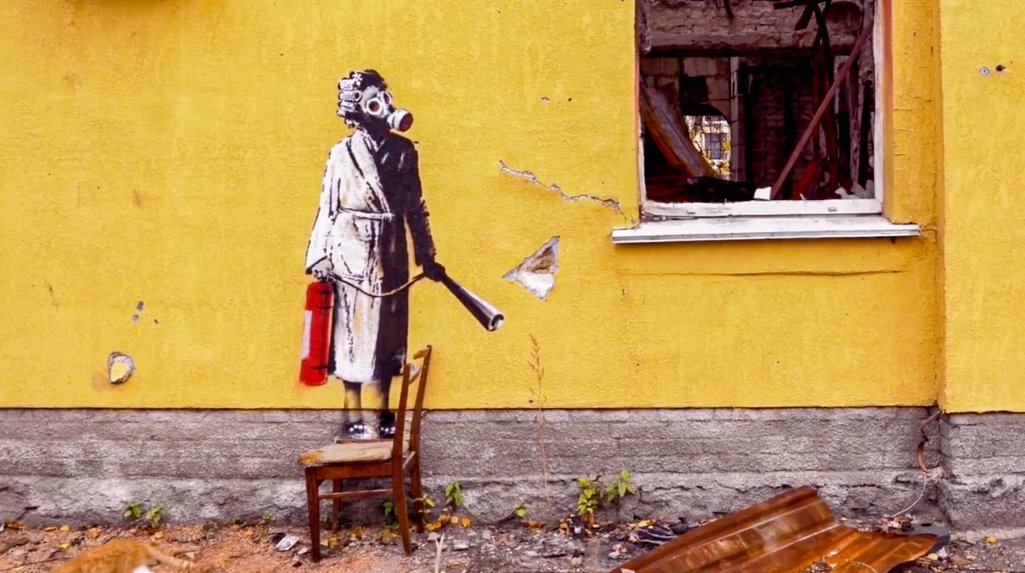 The Banksy has been painted on a yellow wall, it shows a woman in a dressing gown wearing a gas mask