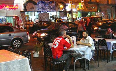 Night scene: cafe tables and chairs encroach into a Cairo street. Two men sit chatting.