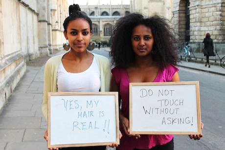 2 Oxford students, women, holding signs that say &#39;Yes, my had is real!!&#39; and &#39;Do not touch without asking!&#39;