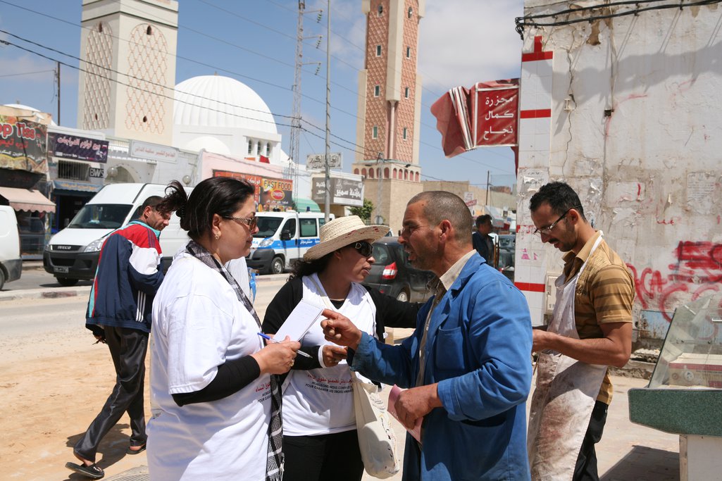 Women talking to men on the street, a mosque in the background