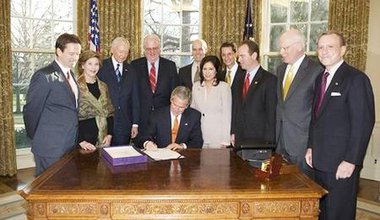 President Bush at a desk in the Oval Office surrounded by politicians and advisors