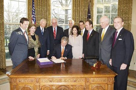 President Bush at a desk in the Oval Office surrounded by politicians and advisors