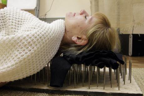 A woman lies on top of a bed of nails in the Alten Centre