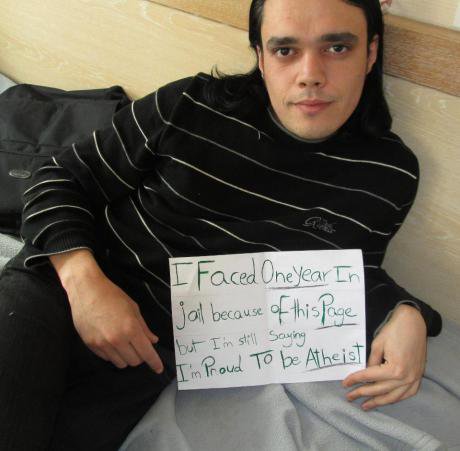 Man holding sign saying 'I faced one year in jail because of this page, but I'm still saying I'm proud to be Atheist'