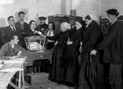 Black and white archive image of 1930s polling station with 4 women lined up to vote.