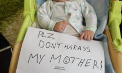 Baby holding a sign reading 'please don't harras my mother'